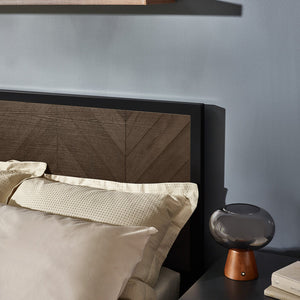Bed with wooden headboard and pillows against a gray wall