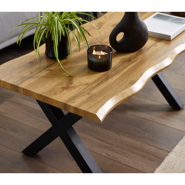 Wooden coffee table with black metal legs, candle, and plant in a room setting.