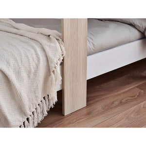 Close-up of a bed with beige bedding and wooden headboard on a wooden floor.