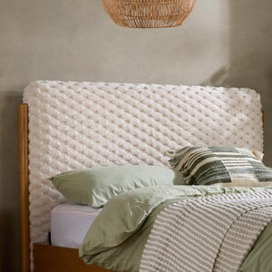Bed with textured headboard and green bedding against a neutral wall.