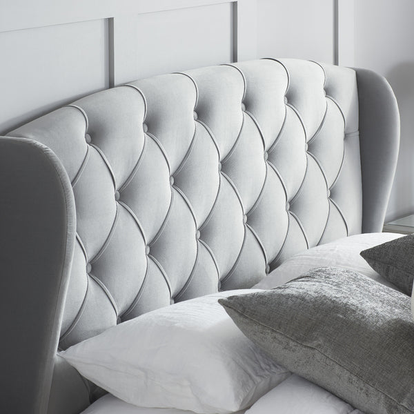 Gray tufted headboard with pillows against a white paneled wall