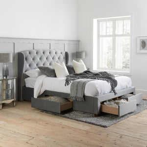 Gray upholstered bed with storage drawers in a bedroom setting.
