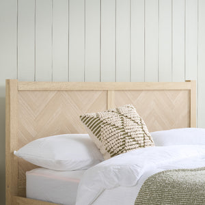 Bed with wooden headboard and decorative pillows against a white paneled wall