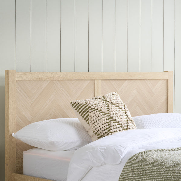 Bed with wooden headboard and decorative pillows against a white paneled wall