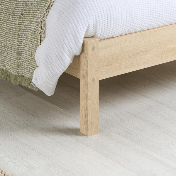 Wooden bed frame with white bedding on a light wooden floor