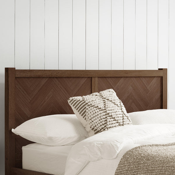 Bed with wooden headboard and textured pillows against a white paneled wall