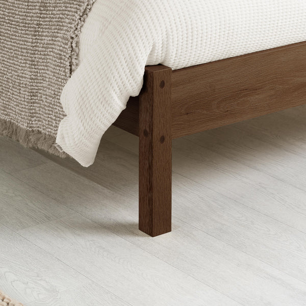 Wooden bed frame with bedding on a light wooden floor