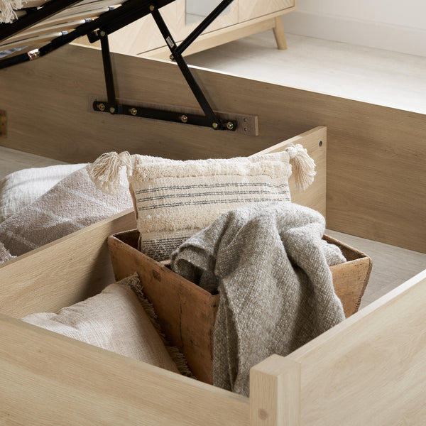 Wooden drawer with pillows and blankets inside, part of a bed setup.