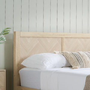 Wooden bed with white bedding and decorative pillows against a light gray wall.
