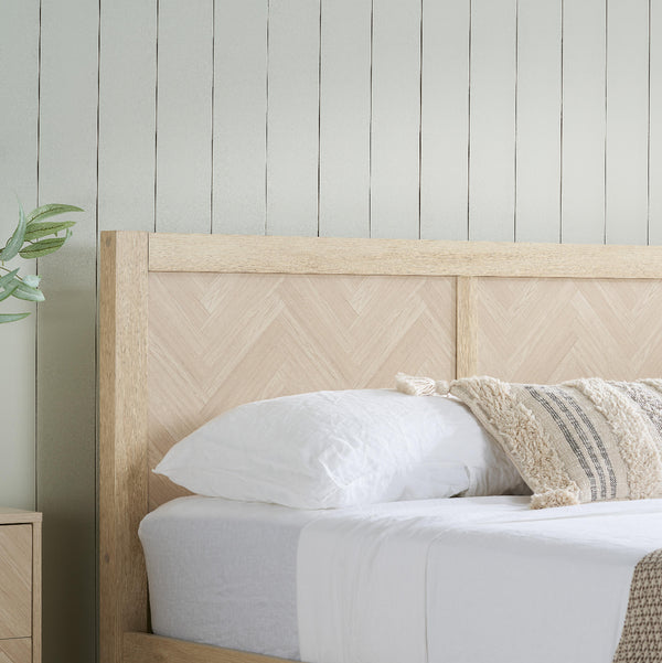 Wooden bed with white bedding and decorative pillows against a light gray wall.
