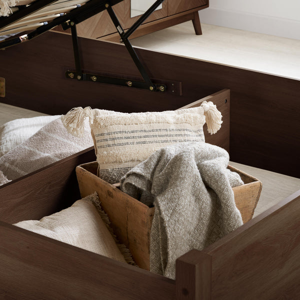 Wooden drawer with pillows and a blanket inside, part of a bed setup.