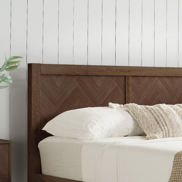 Bed with wooden headboard and white bedding against a white paneled wall.
