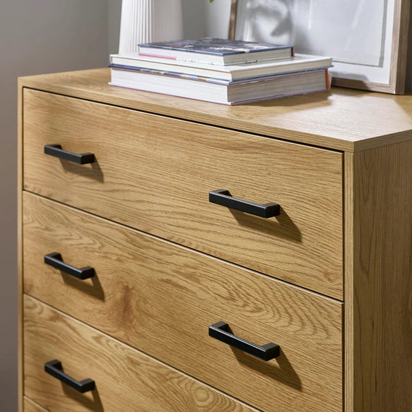 Wooden dresser with four drawers and black handles, featuring a stack of books on top.