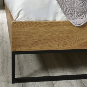 Wooden bed frame with a mattress and gray quilt on a wooden floor.
