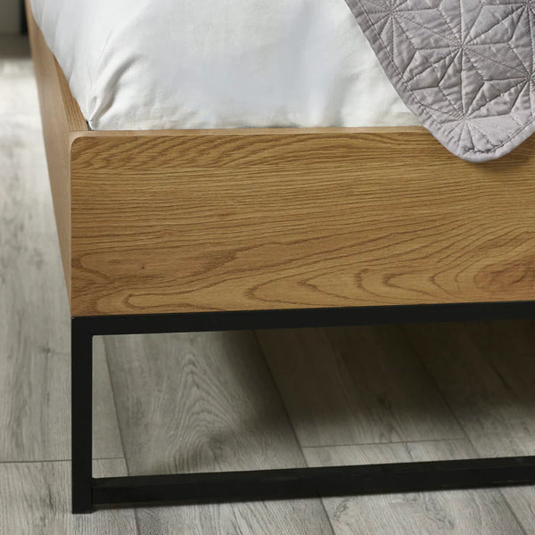 Wooden bed frame with a mattress and gray quilt on a wooden floor.