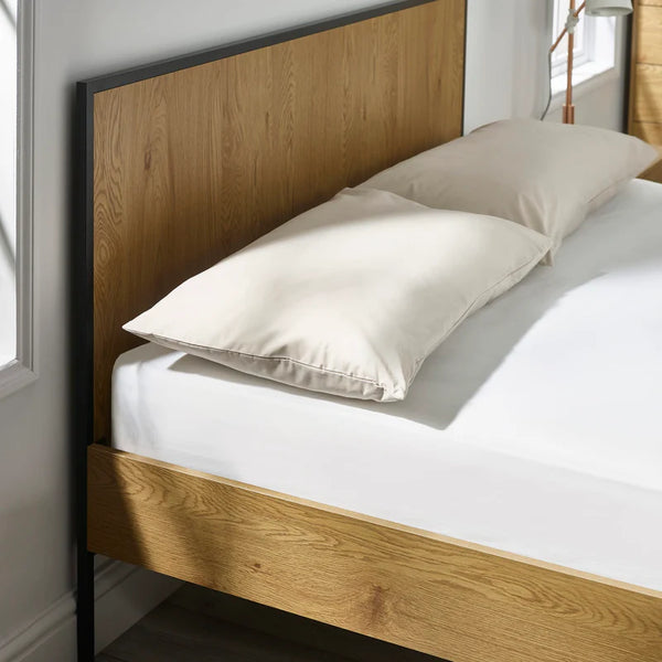 Wooden bed frame with white bedding and pillows in a bedroom setting