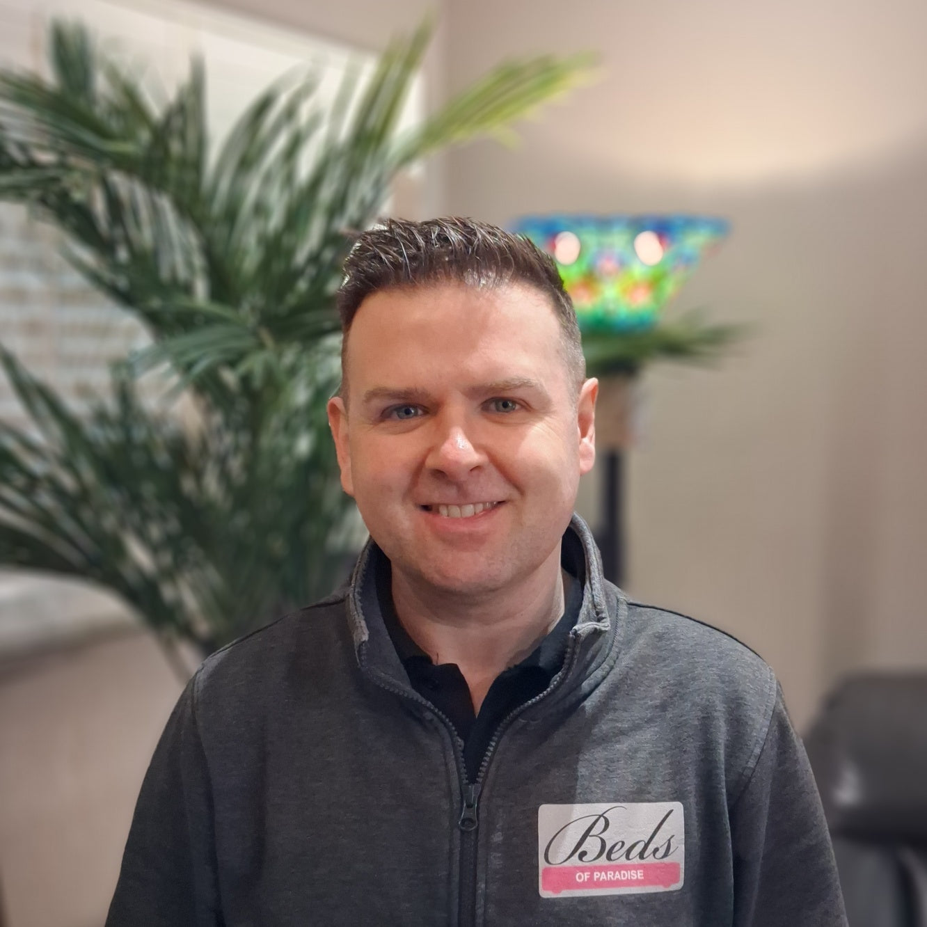 Man wearing a branded jacket with a plant and colorful lamp in the background
