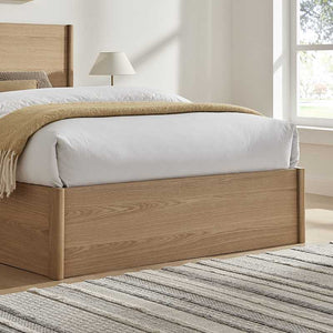 Wooden bed with white bedding and a beige blanket in a bright bedroom.