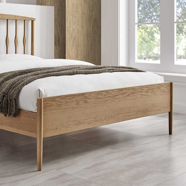 Wooden bed with white bedding and a brown throw in a room with large windows.