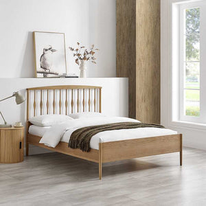 Wooden bed in a bedroom with a lamp, vase, and framed picture on a white wall.