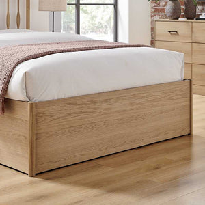 Wooden bed frame with white bedding in a room with a window and dresser.