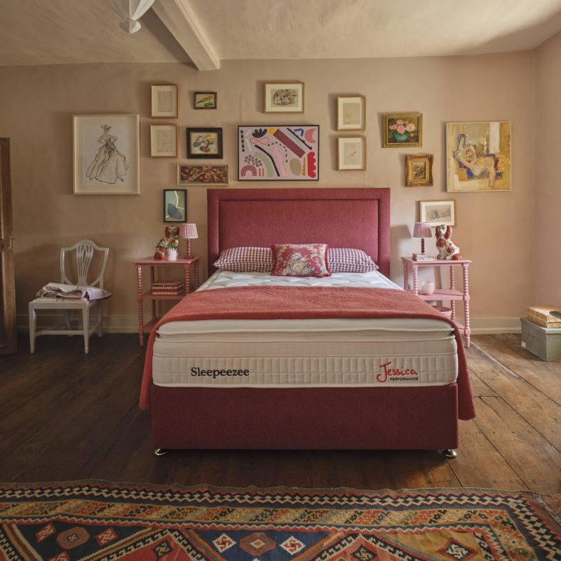 Bedroom with a red bed frame and mattress, surrounded by framed artwork on the walls.