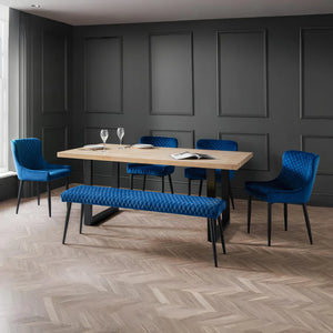 Modern dining room with wooden table, blue chairs, and a bench against a gray paneled wall.