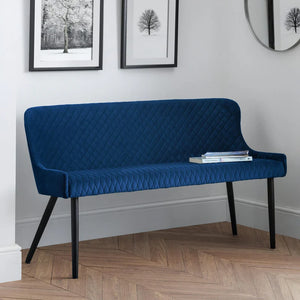 Blue quilted bench in a room with framed pictures on the wall.