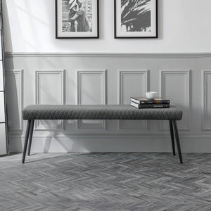 Gray upholstered bench in a room with framed pictures on the wall.