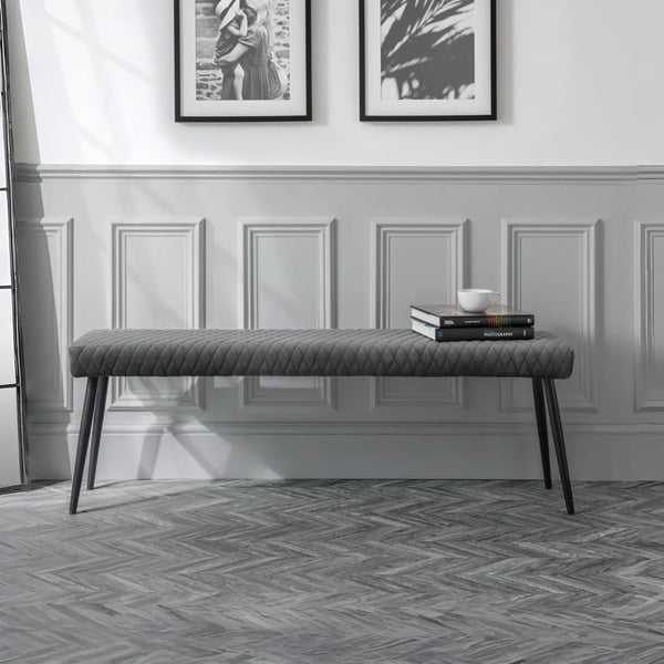 Gray upholstered bench in a room with framed pictures on the wall.