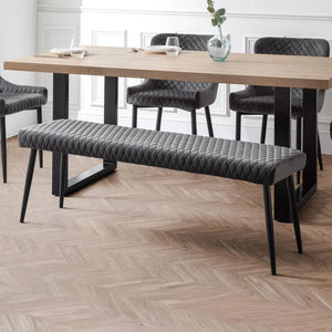 Dining room with a wooden table and gray upholstered bench on a herringbone wood floor.