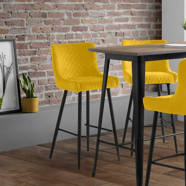 Yellow bar stools with black legs around a wooden table against a brick wall.
