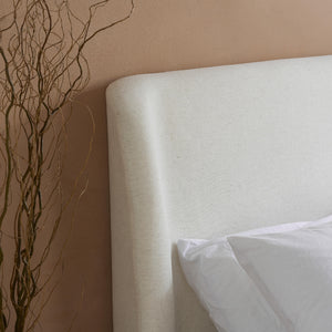 Mattress with a white pillow against a beige wall with decorative branches.
