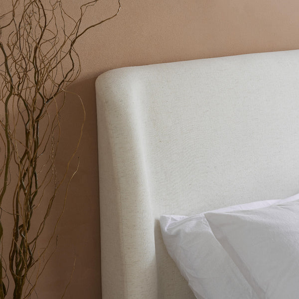 Mattress with a white pillow against a beige wall with decorative branches.