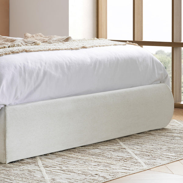 White bed with beige bedding in a room with large windows.