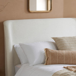 Neatly made bed with white pillows and a beige headboard against a beige wall.