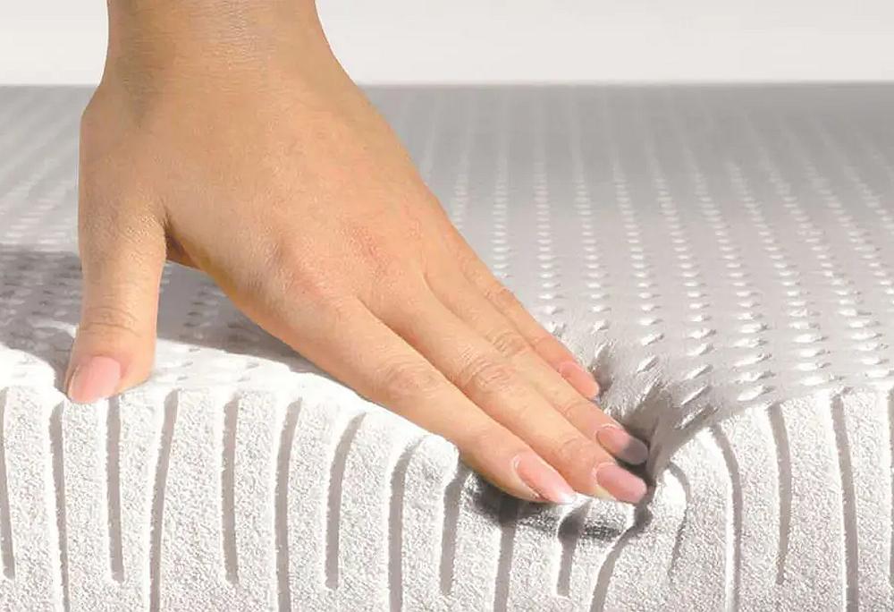 Hand pressing down on a mattress surface to demonstrate firmness.