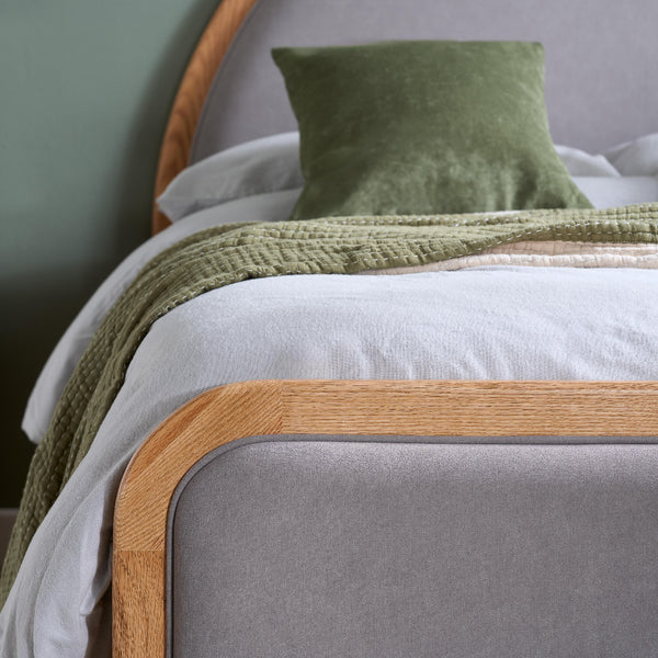 Gray bed with wooden headboard and green blanket and pillow