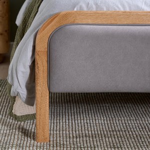 Gray upholstered bed with wooden frame on a textured carpet