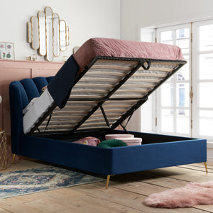 Blue upholstered bed with storage compartment open in a room with white walls and large windows.