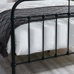 Black metal bed frame with white bedding and a dark gray blanket on a wooden floor.