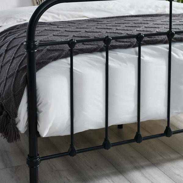 Black metal bed frame with white bedding and a dark gray blanket on a wooden floor.