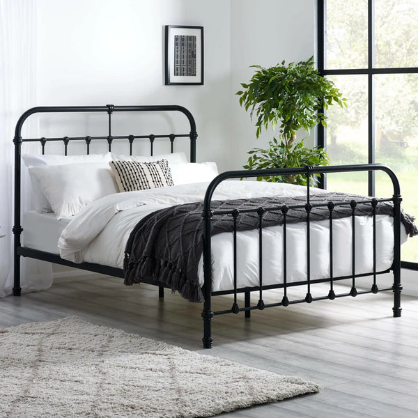 Black metal bed frame with white bedding in a room with a large window and plant.
