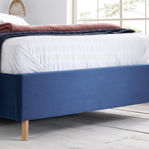 Blue bed frame with white bedding and pink blanket in a bright room.