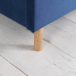 Close-up of a blue upholstered bed leg on a light wooden floor