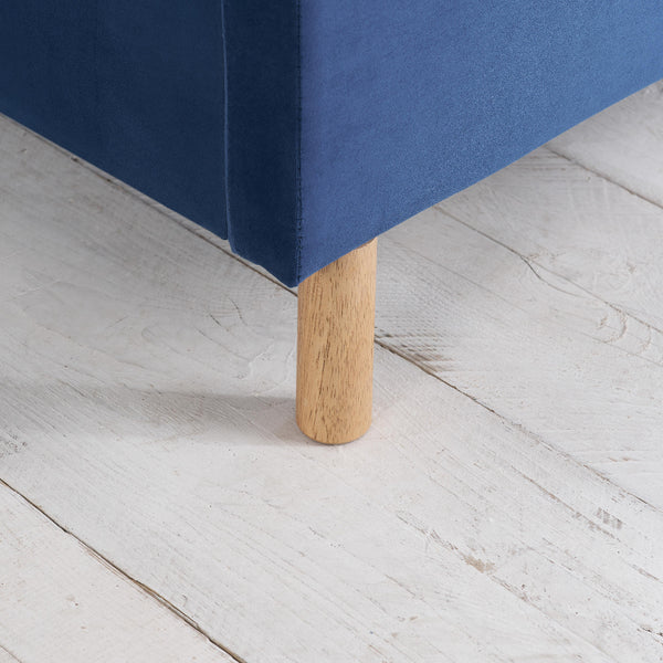 Close-up of a blue upholstered bed leg on a light wooden floor