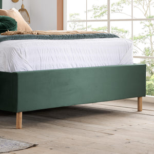Green bed frame with white bedding in a room with large windows.