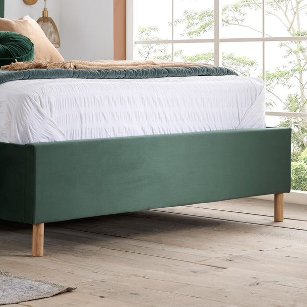 Green bed frame with white bedding in a room with large windows.