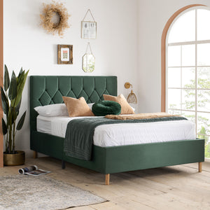 Green upholstered bed in a bright bedroom with large windows and decorative elements.