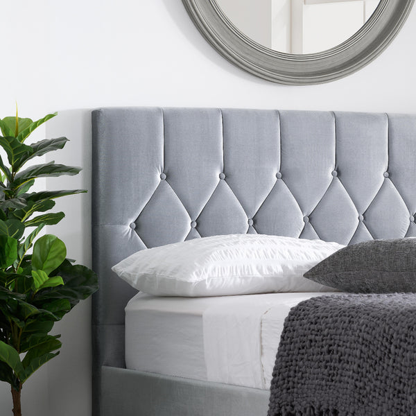 Gray upholstered headboard with pillows and a plant in a bedroom setting